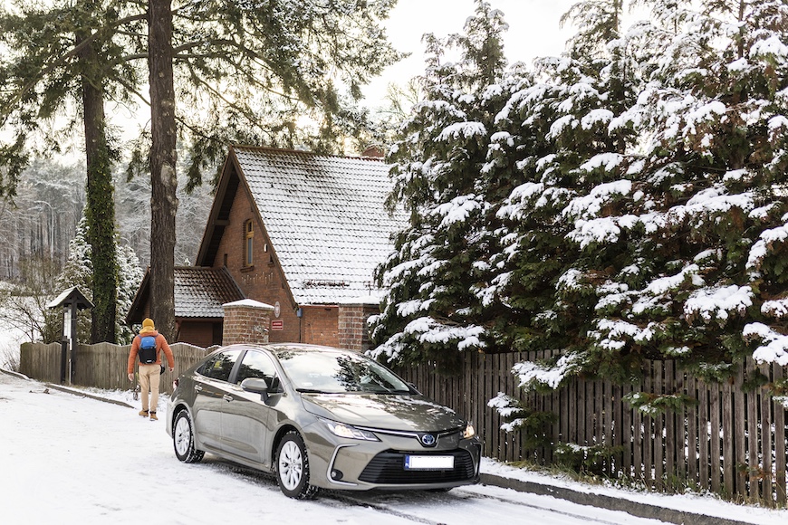 Samochód w zimowej scenerii na tle ośnieżonego domu i drzew